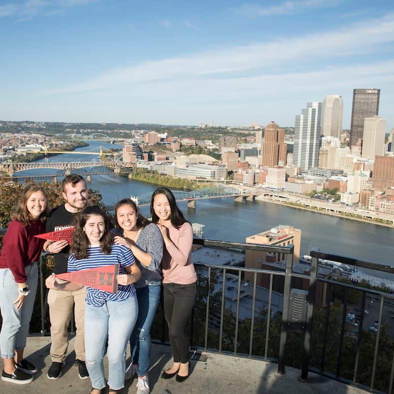 Students pose with a pennant as they look out over the city of Pittsburgh from Mount Washington October 21, 2019 during the Creosote Affects photo shoot at Washington &amp; Jefferson College.